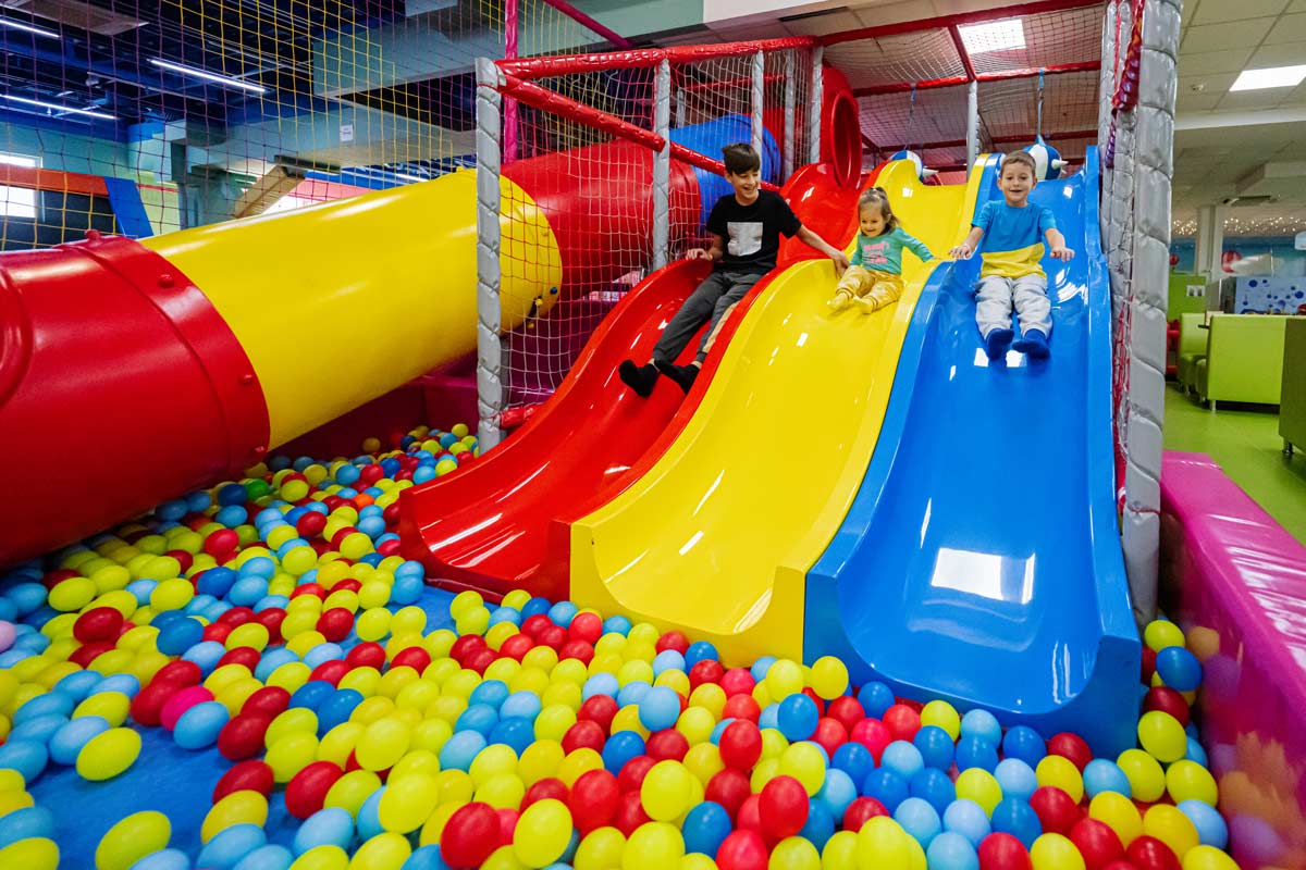 Gruppe von Kindern auf einem Kindergeburtstag im Indoor-Spielplatz beim rutschen in ein Bällebad