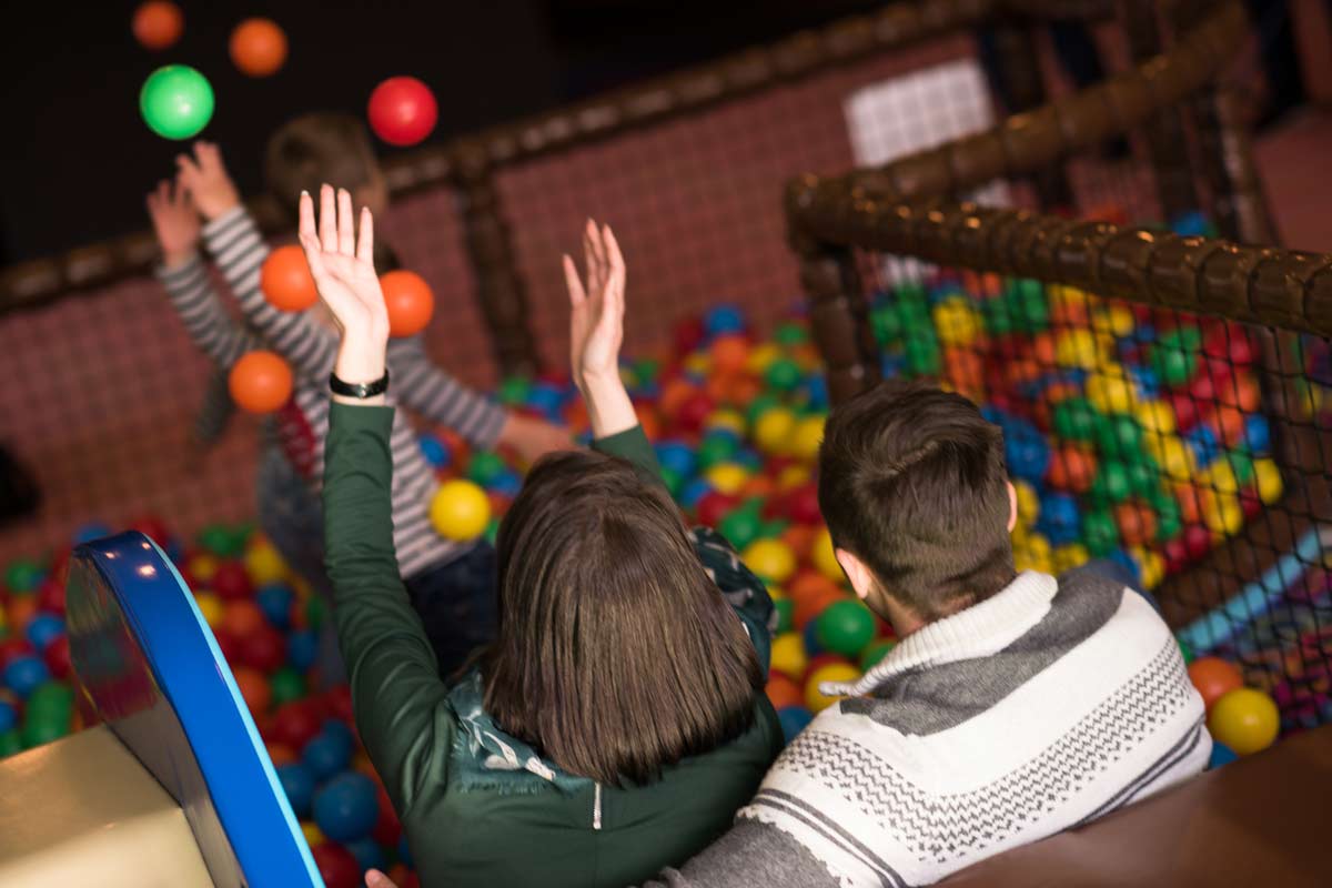 Eltern bei einem Kindergeburtstag im Indoorspielplatz, die aufpassen und beim spielen zuschauen